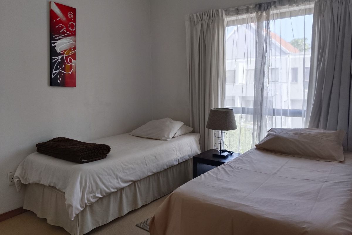 A functional bedroom featuring a large window with natural light, neutral wall finishes, and carpeted flooring.