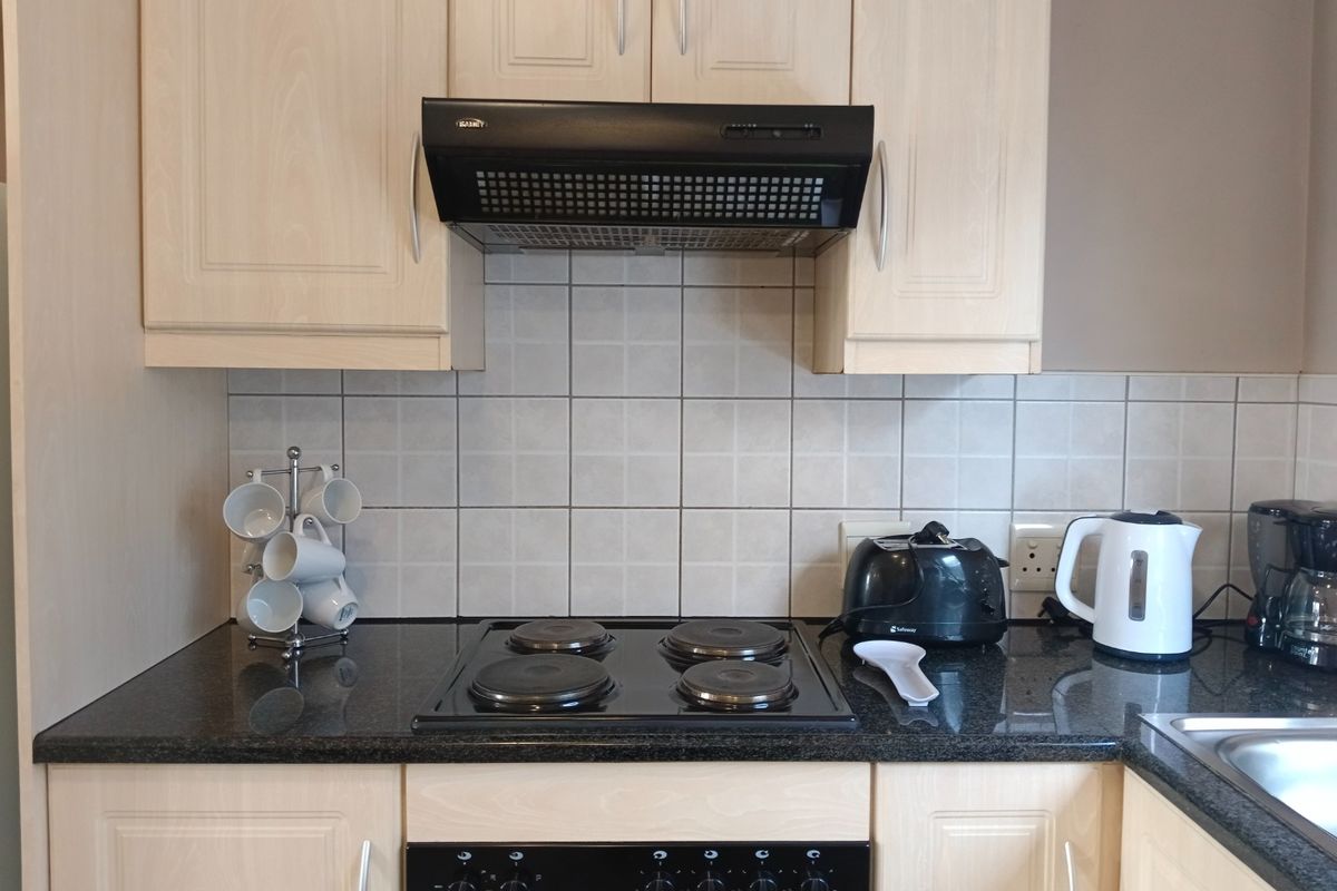 A functional kitchen area featuring light wood-finish cabinetry, dark granite countertops, a ceramic tile backsplash, and integrated cooking appliances.