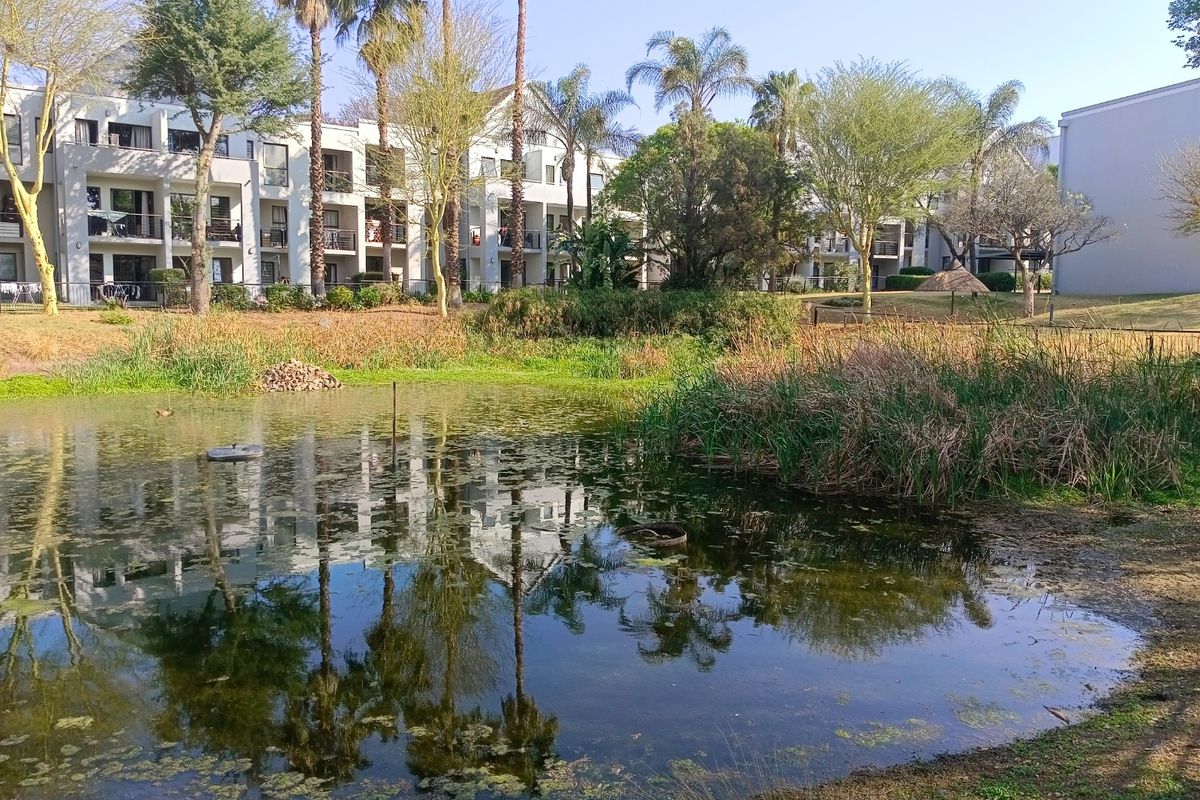 A view of the apartment complex exterior featuring a natural pond, landscaped garden areas, and private balconies overlooking the grounds.