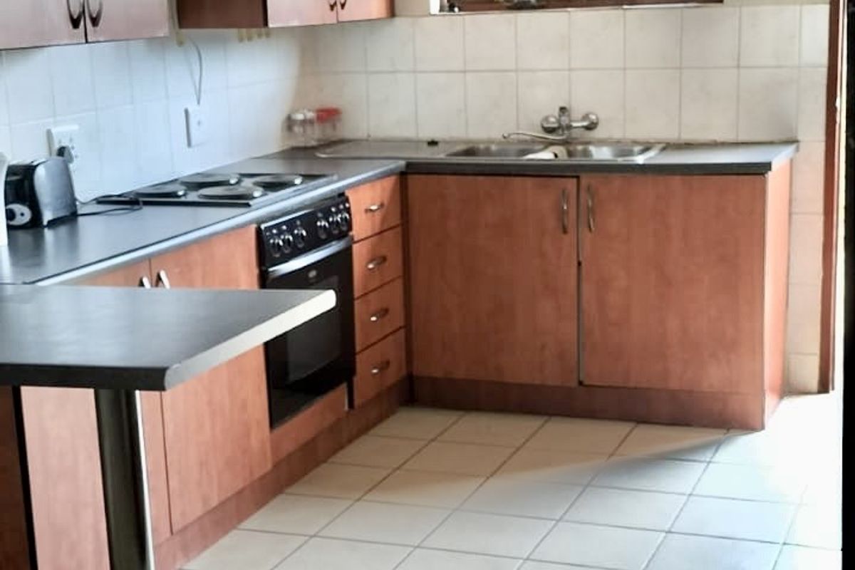 A functional kitchen featuring wood-look cabinetry, built-in oven, electric hob, and tiled flooring with a breakfast bar extension.