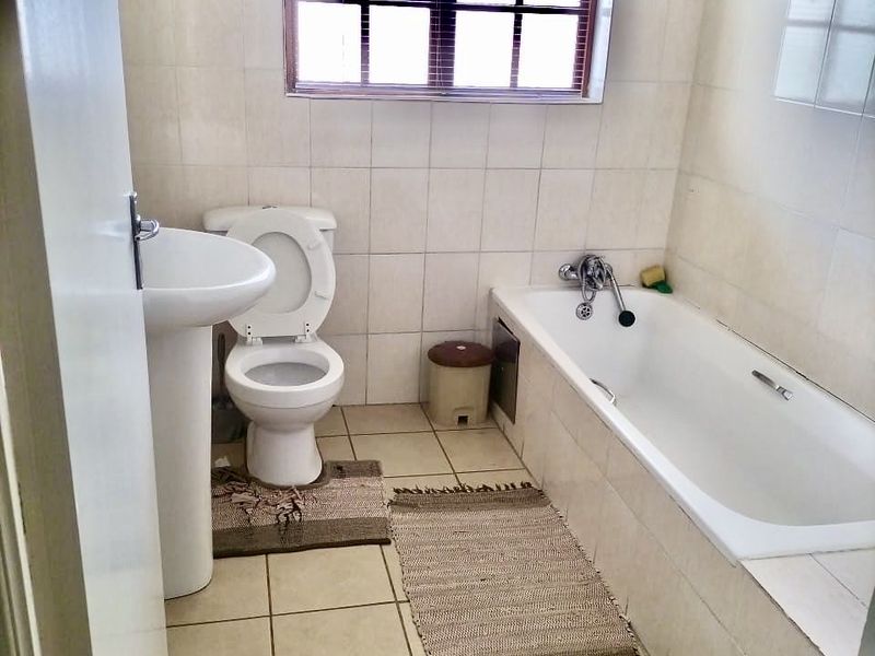 A functional bathroom featuring a pedestal basin, toilet, and bathtub with tiled finishes throughout.