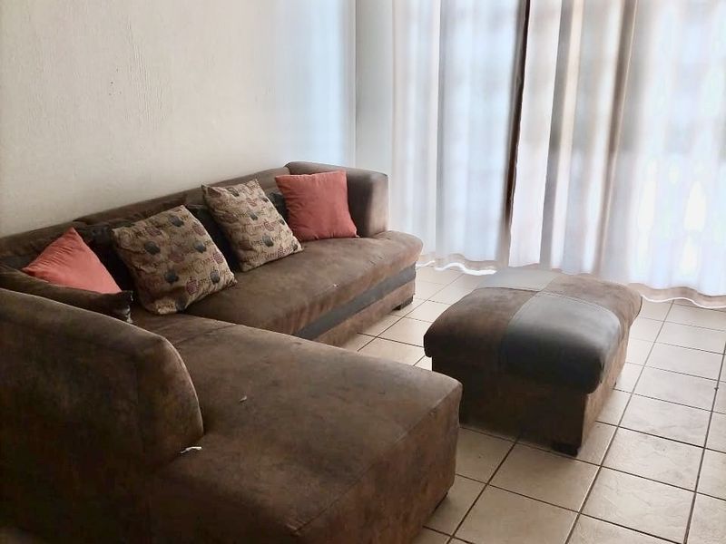 A living room area featuring neutral tiled flooring and a large window with curtain fixtures, providing a functional and well-lit space.