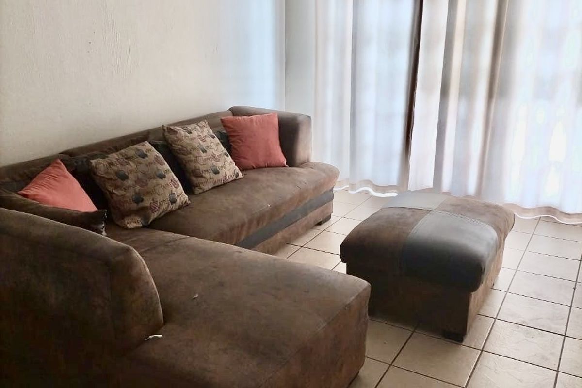 A living room area featuring neutral tiled flooring and a large window with curtain fixtures, providing a functional and well-lit space.