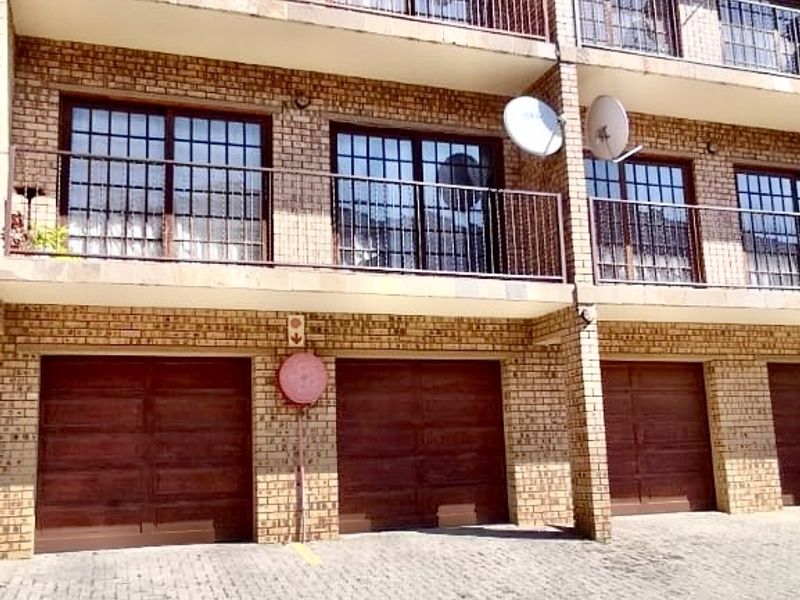 Exterior view of a multi-story apartment building featuring brick facade, private balconies with metal railings, and ground-level garage access with paved driveway.