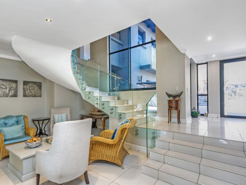 Elegant entrance foyer featuring a modern glass-railed staircase, tiled flooring, and a striking floor-to-ceiling window that floods the space with natural light.