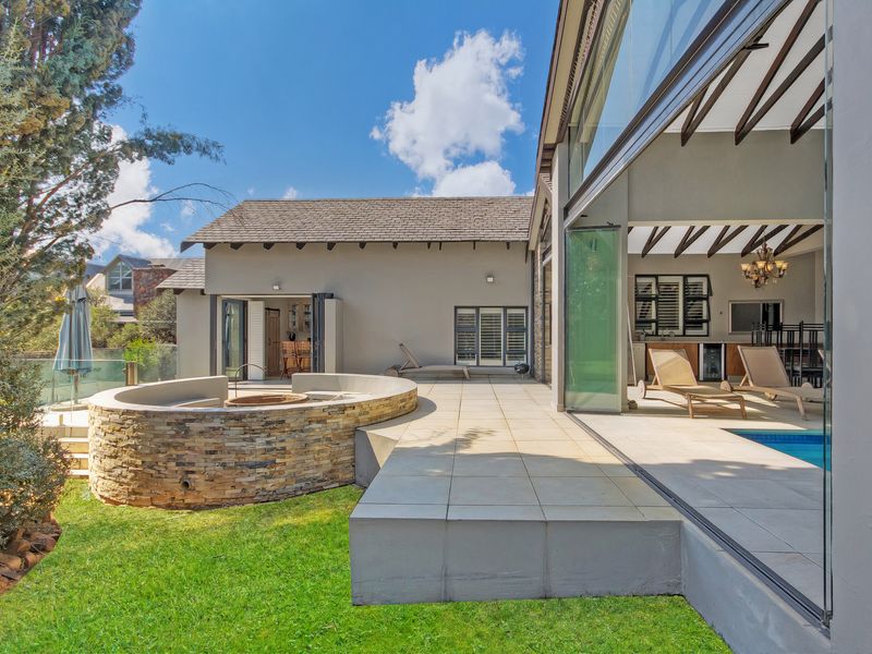 A beautifully maintained rear patio featuring a stone-clad fire pit, seamless indoor-outdoor flow through stacking doors, and a private swimming pool.