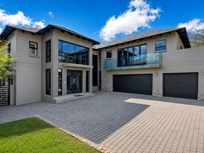 Modern double-story residence featuring a paved driveway, double garage, and a glass-balustrade balcony, showcasing contemporary architectural design and well-maintained exterior finishes.