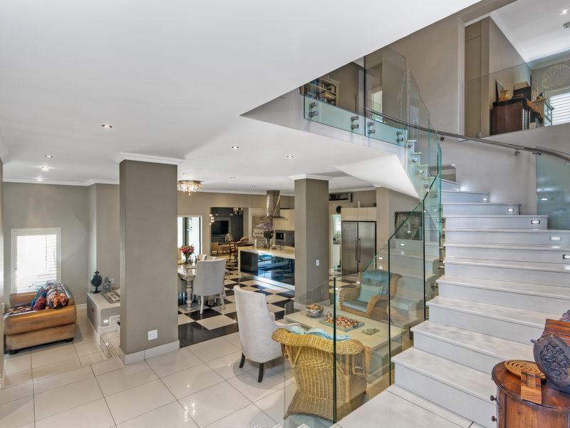 Spacious open-plan living area featuring a modern glass-railed staircase, tiled flooring, and a contemporary kitchen with a central island.