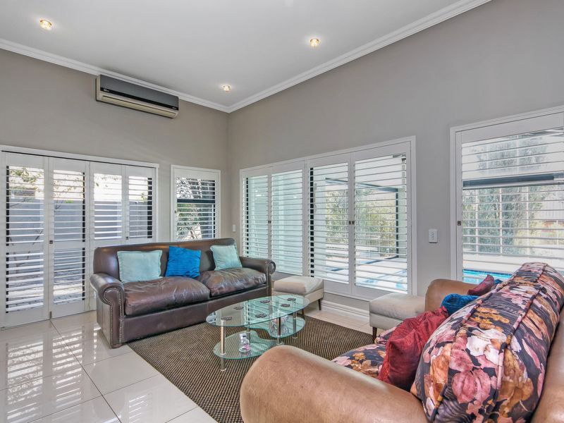 Bright living room featuring tiled flooring, recessed downlights, crown molding, and plantation shutters with views of the pool area.