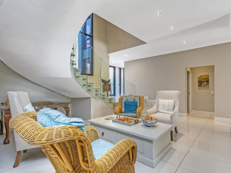 A bright living area featuring a striking curved staircase with a modern glass balustrade and polished floor tiles.