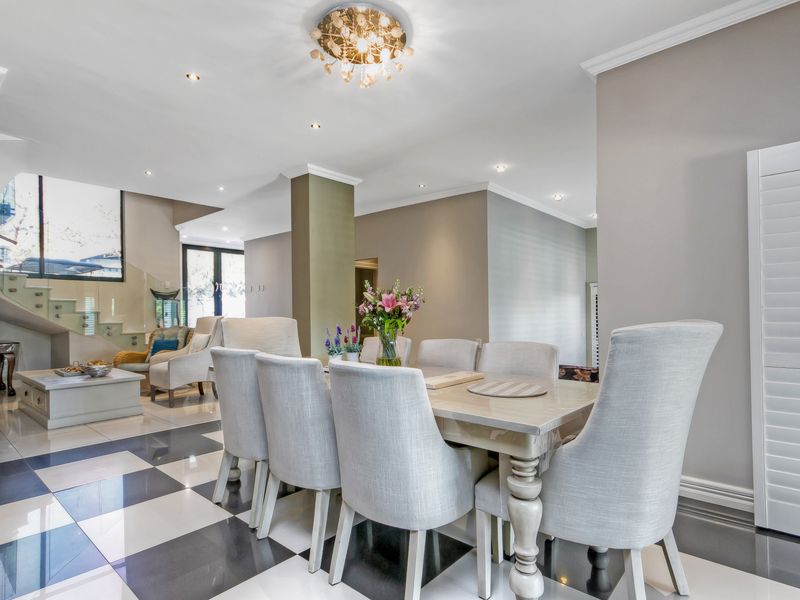 Spacious open-plan dining and living area featuring high-end porcelain checkered flooring, modern recessed lighting, and an elegant glass balustrade staircase.