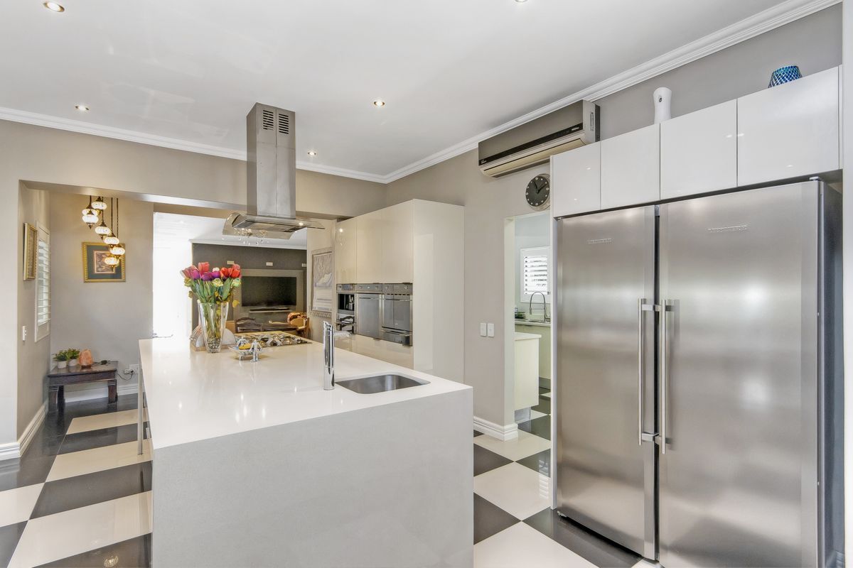 Modern kitchen featuring a large stone island, stainless steel appliances, built-in ovens, and sleek cabinetry with a checkerboard tiled floor.