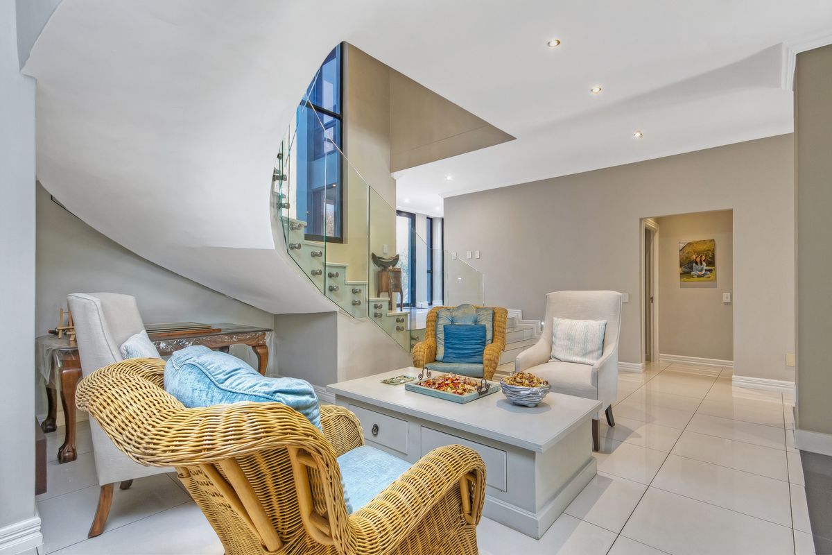 A bright living area featuring a striking curved staircase with a modern glass balustrade and polished floor tiles.