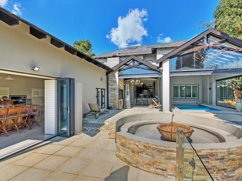Spacious rear patio featuring a built-in stone fire pit, swimming pool, and seamless indoor-outdoor flow through large stacking glass doors.