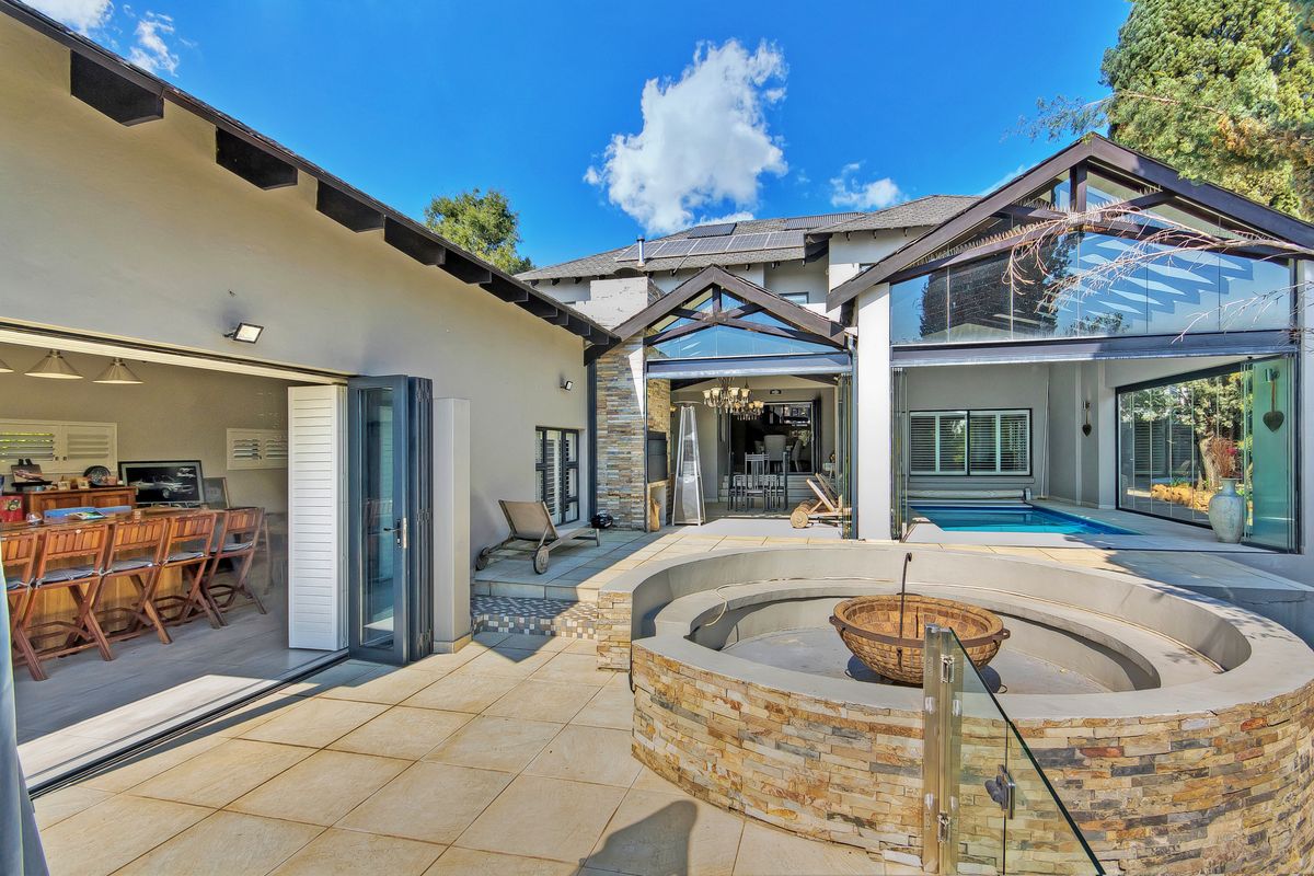 Spacious rear patio featuring a built-in stone fire pit, swimming pool, and seamless indoor-outdoor flow through large stacking glass doors.