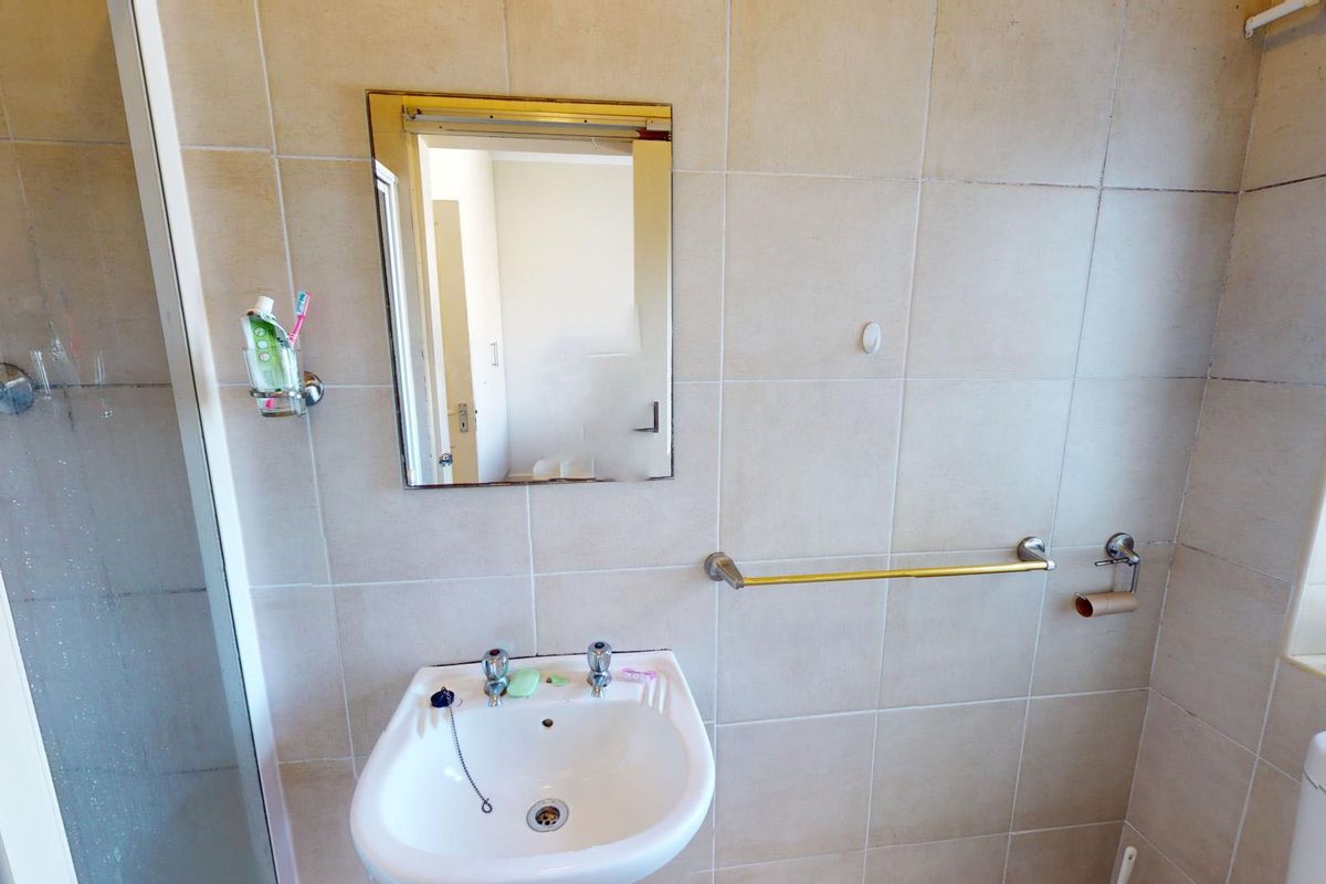 A functional bathroom featuring a wall-mounted basin, shower enclosure, and neutral wall tiling, offering a practical layout with standard fixtures.