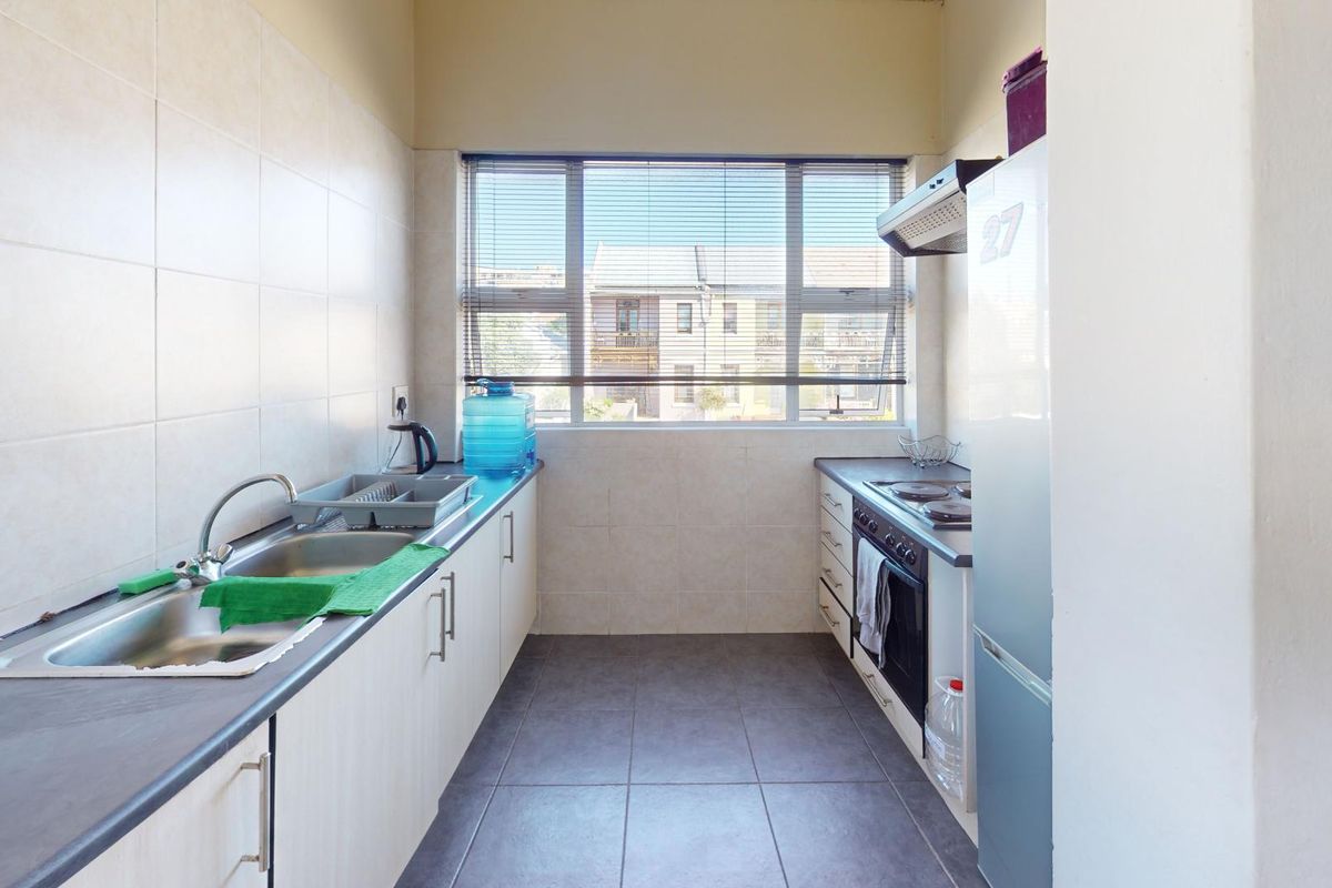 A functional galley-style kitchen featuring built-in cabinetry, a stainless steel sink, integrated oven and hob, and tiled finishes throughout.
