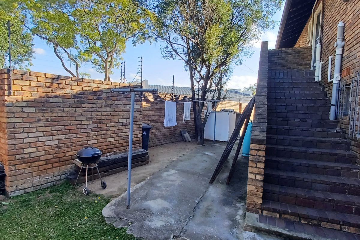 Rear exterior view of the apartment featuring a brick staircase, perimeter wall with electric fencing, and a paved courtyard area.