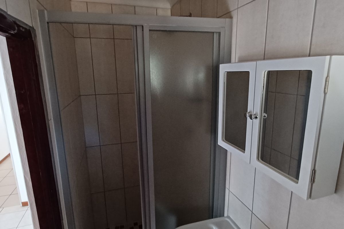 A functional bathroom featuring a tiled shower enclosure and a wall-mounted medicine cabinet, showing standard wear and dated finishes.
