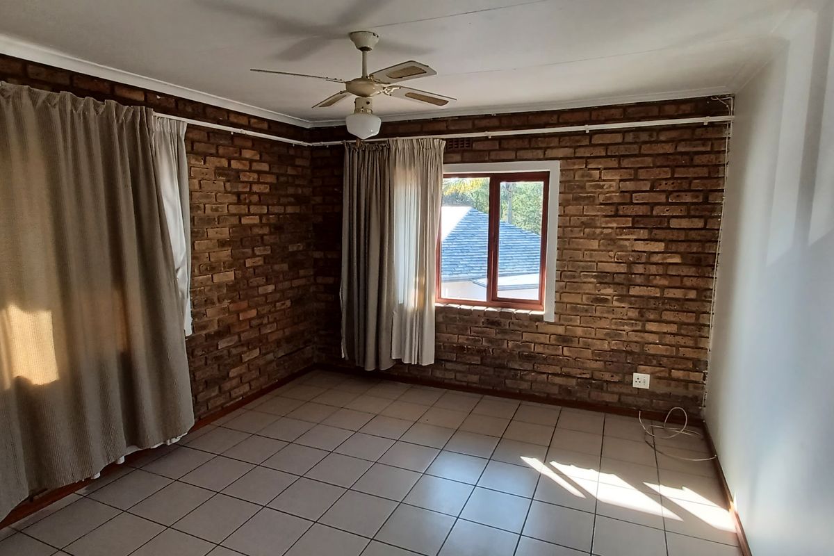 A spacious bedroom featuring exposed brick walls, tiled flooring, and a ceiling fan.