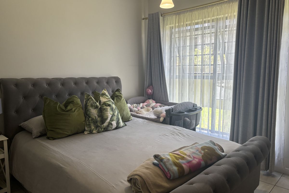 A well-lit bedroom featuring tiled flooring, a large sliding glass door with security gate, and neutral wall finishes.