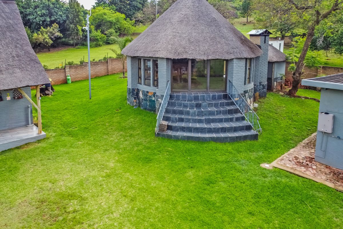 A well-maintained circular cottage featuring a traditional thatched roof, stone base detailing, and slate stairs leading to glass sliding doors in a garden setting.