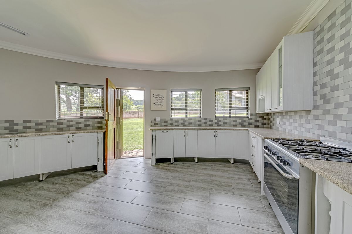 A bright, spacious kitchen featuring white cabinetry, granite countertops, a gas stove, and a tiled backsplash with direct access to the garden.