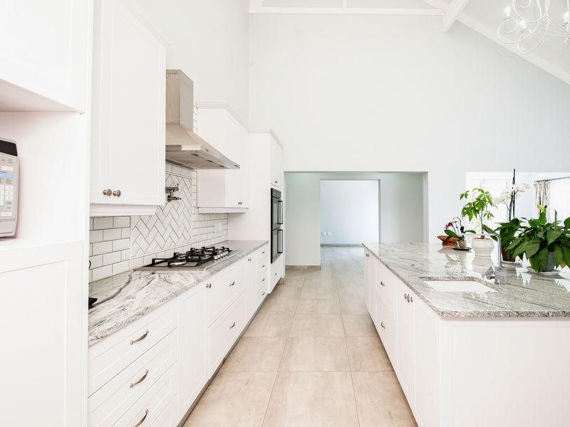Modern kitchen featuring white cabinetry, granite countertops, a central island, gas hob, and high vaulted ceilings with a bright, open layout.