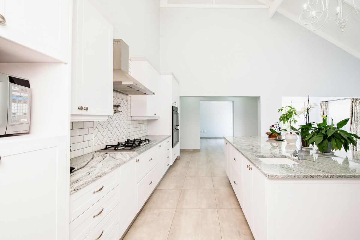 Modern kitchen featuring white cabinetry, granite countertops, a central island, gas hob, and high vaulted ceilings with a bright, open layout.