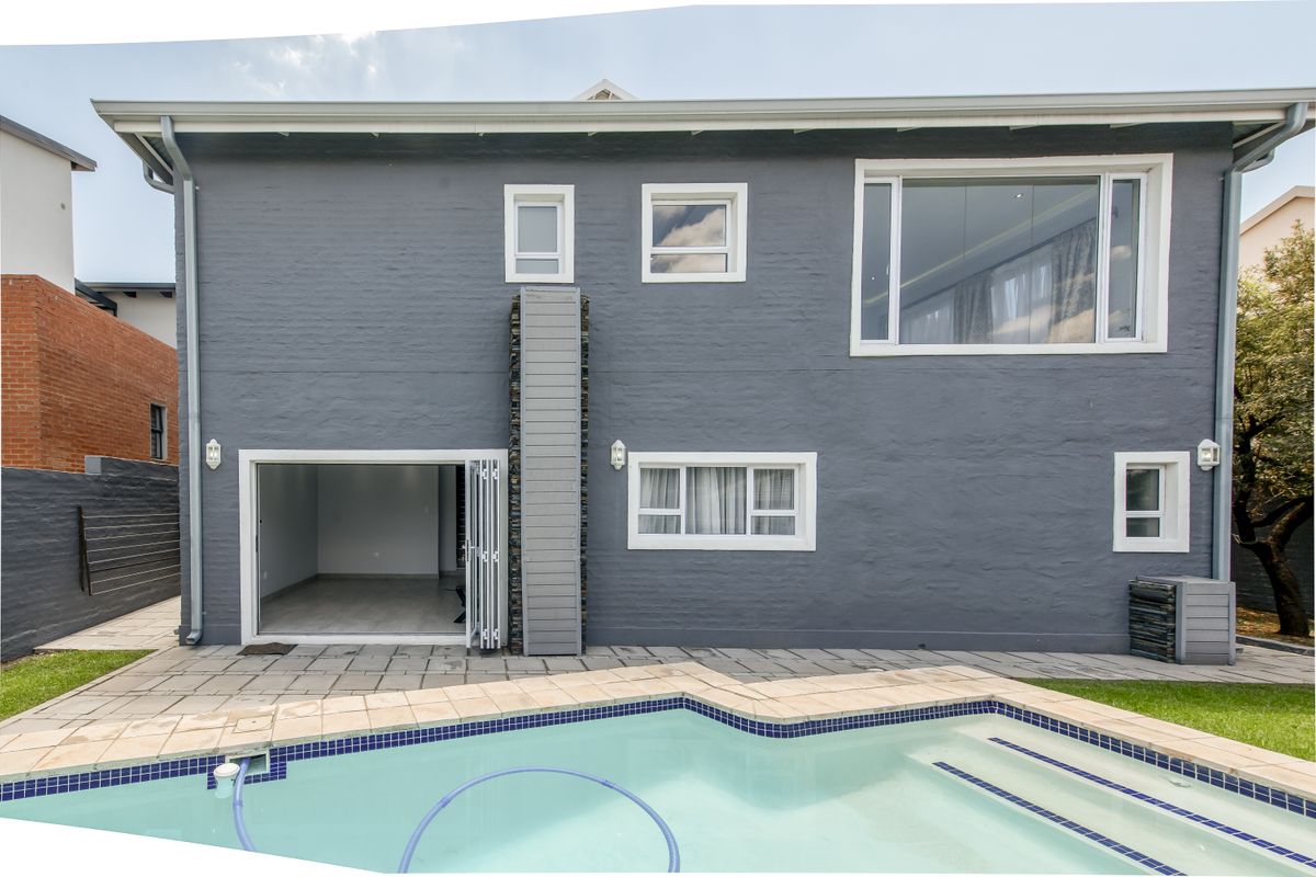 Rear elevation of a two-story house featuring a swimming pool, paved patio area, and modern bi-fold doors leading into the interior living space.