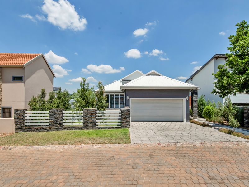 Front elevation of a modern house featuring a paved driveway, double garage, and a decorative stone-clad boundary wall.