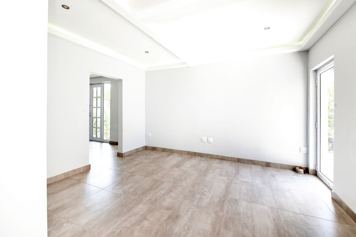 A bright, empty living area featuring modern tiled flooring, recessed ceiling lighting, and access to outdoor spaces through glass sliding and french doors.