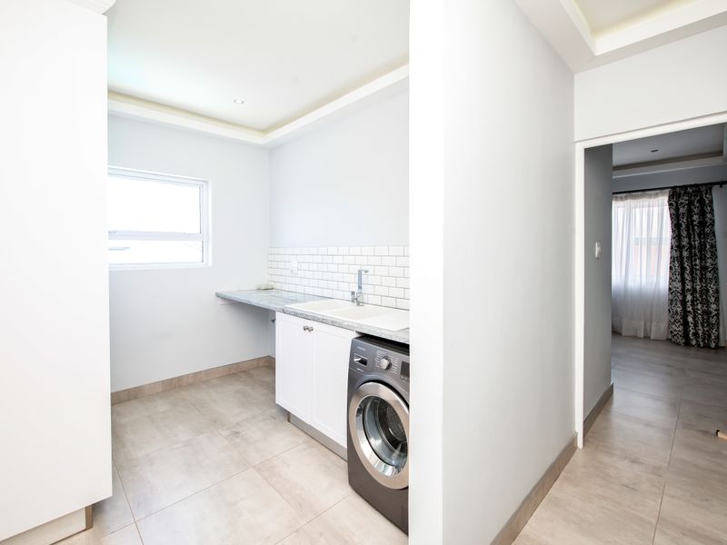 A clean and functional laundry area featuring built-in cabinetry, granite countertops, an undermount sink, and modern subway tile backsplash.