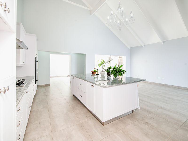 Spacious modern kitchen featuring a large central island with granite countertops, built-in appliances, and high vaulted ceilings with neutral finishes.