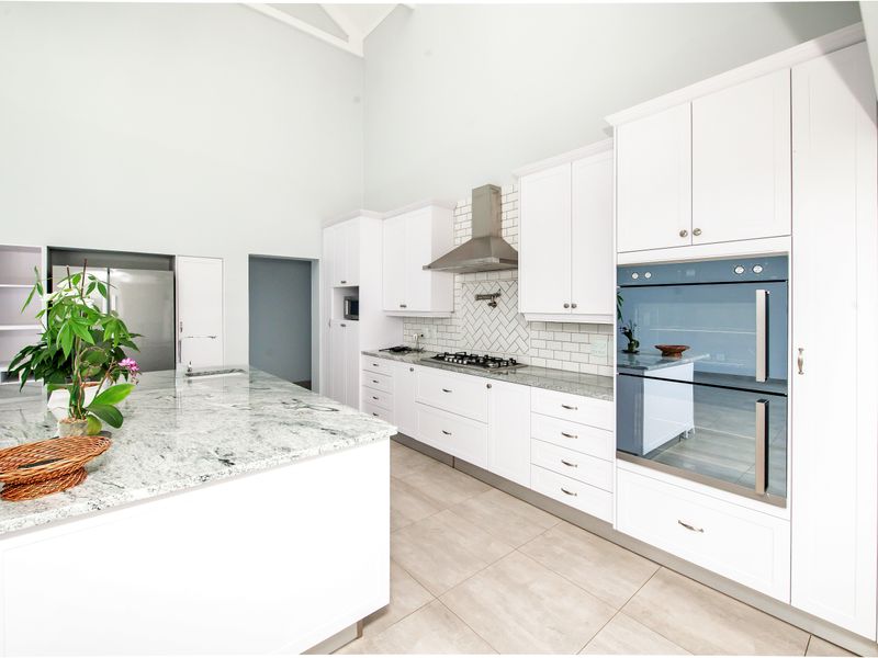 Modern kitchen featuring white shaker cabinetry, granite countertops, a central island, built-in double oven, gas hob, and a stylish herringbone subway tile backsplash.