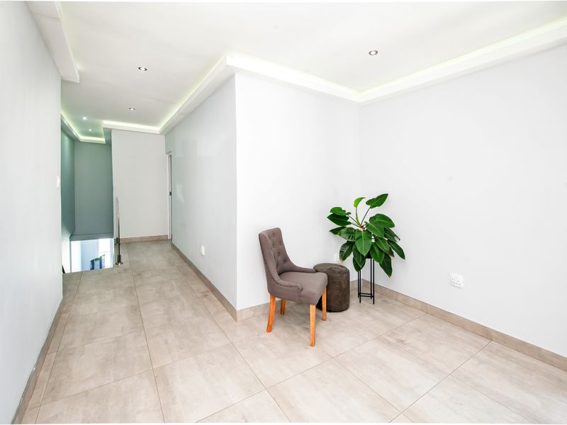 A bright and modern hallway featuring neutral tiled flooring, recessed downlighting, and clean architectural lines.