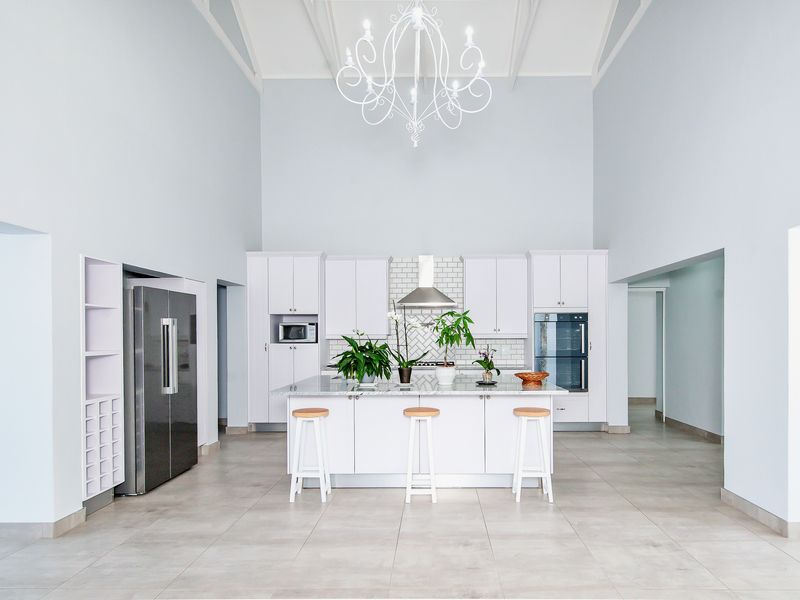 Spacious modern kitchen featuring a large central island, white cabinetry, subway tile backsplash, built-in appliances, and a high vaulted ceiling with elegant lighting.