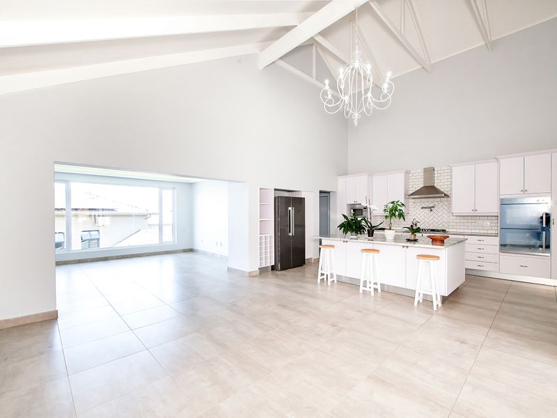 Spacious open-plan living area featuring a modern kitchen with stone countertops, subway tile backsplash, built-in appliances, and a high vaulted ceiling with exposed rafters.