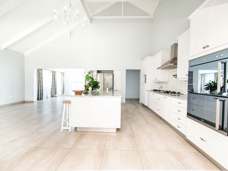 Spacious open-plan kitchen featuring a large island, modern built-in appliances, shaker cabinetry, and high vaulted ceilings with elegant lighting.