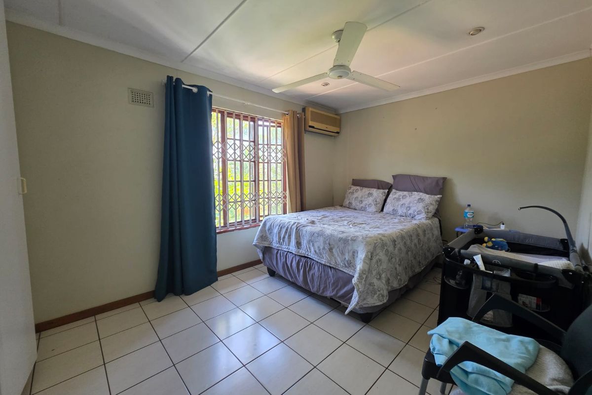 A functional bedroom featuring tiled flooring, a ceiling fan, and a wall-mounted air conditioning unit with security bars on the window.
