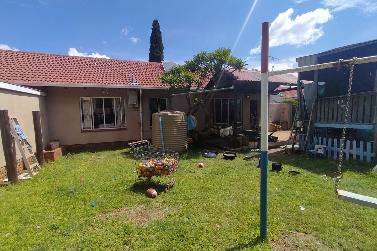 Rear view of the property featuring a tiled roof, a water storage tank, and a garden area with a covered patio.