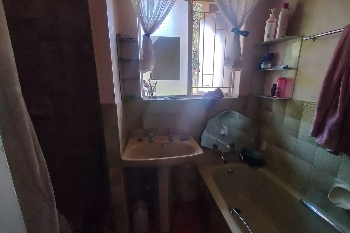 A dated bathroom featuring a pedestal basin, bathtub, and tiled walls, requiring modernization to improve its aesthetic and functionality.