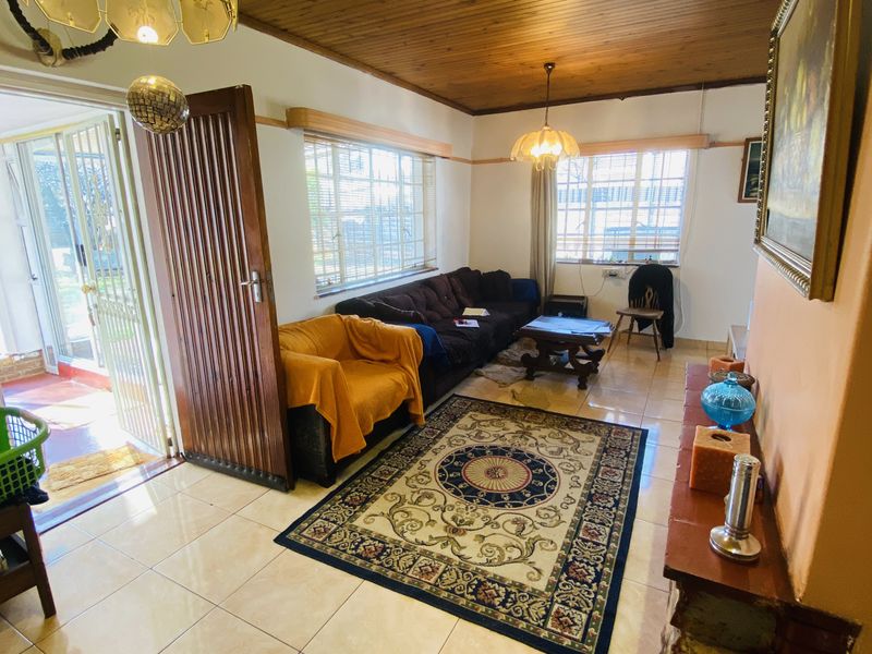 A living room featuring a timber tongue and groove ceiling, ceramic tiled flooring, and a stone-clad fireplace hearth with access to an outdoor area.