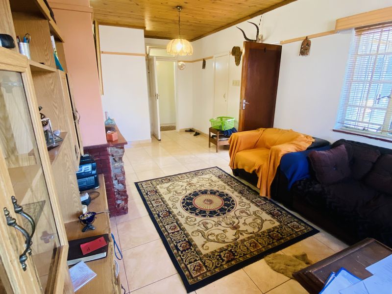 A living room featuring a timber-clad ceiling, ceramic tiled flooring, and a brick fireplace surround, offering a dated but functional living space.