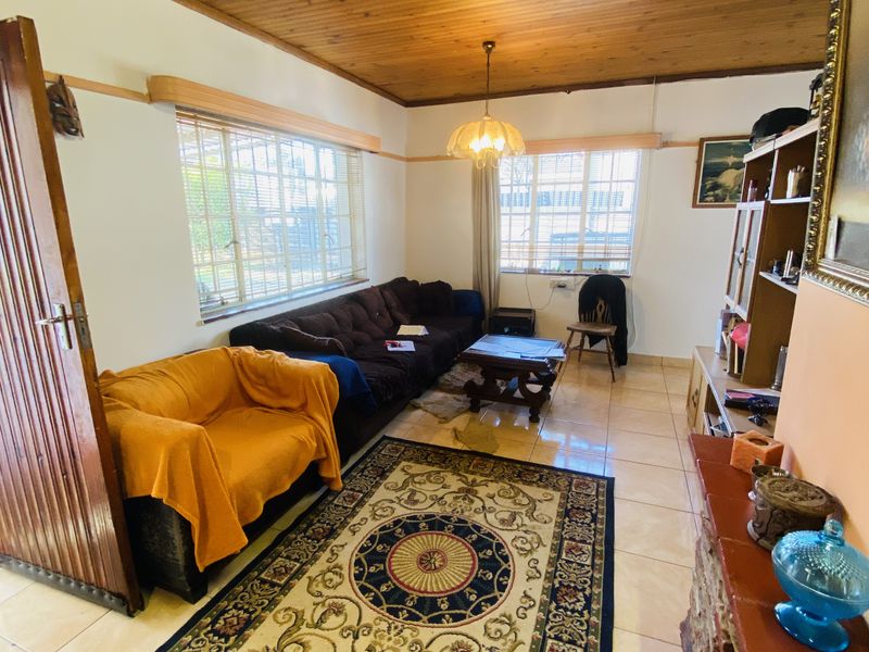 A living room featuring a timber-clad ceiling, tiled flooring, and a stone-clad fireplace, offering a traditional aesthetic with potential for modern updates.