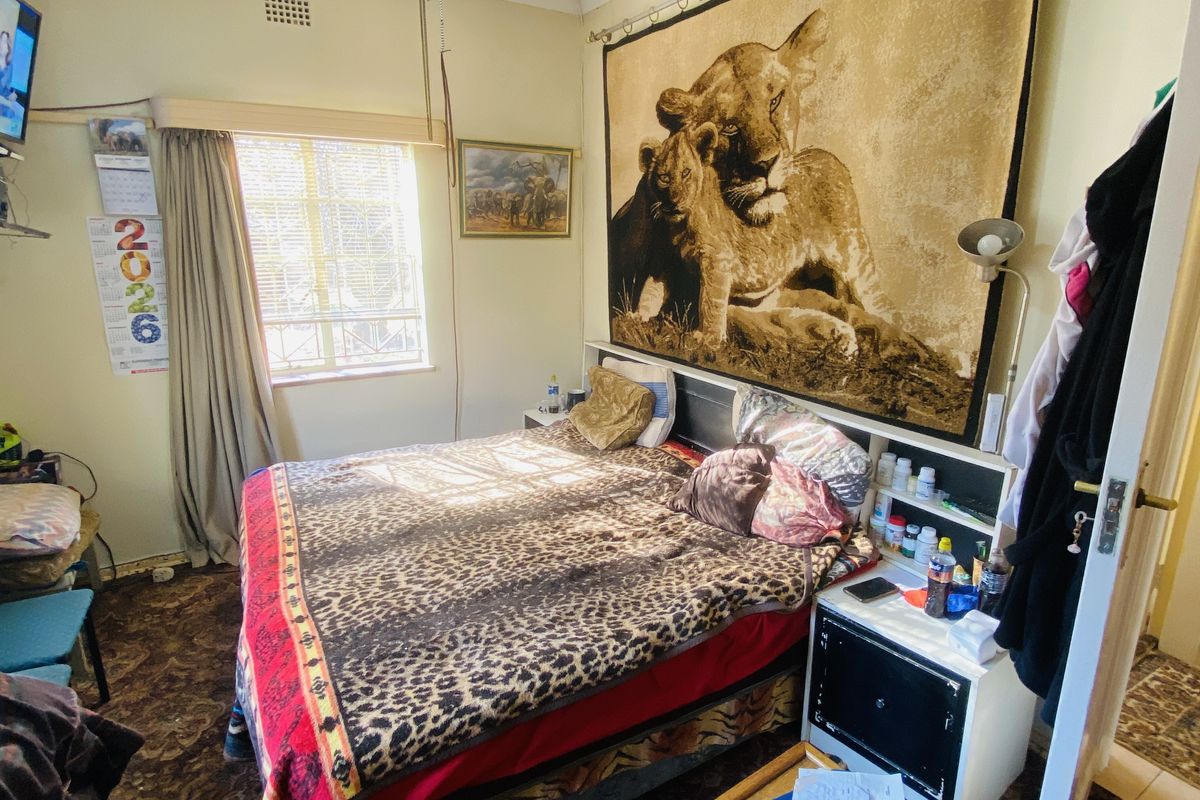 A bedroom featuring a ceiling fan, built-in headboard, and window. The room requires cosmetic updates to the flooring and ceiling finishes.