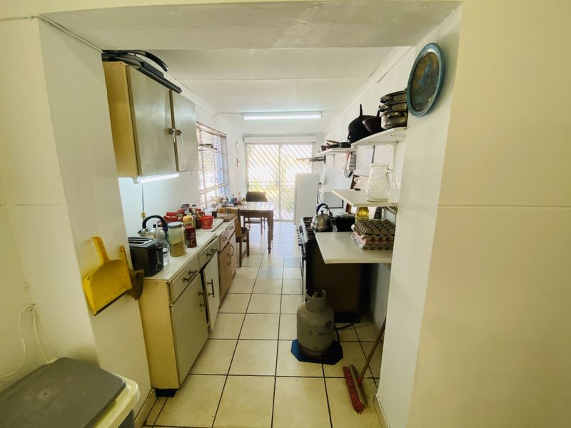 A functional galley-style kitchen featuring tiled flooring, built-in cabinetry, and a gas stove, with direct access to an outdoor area through a sliding door.