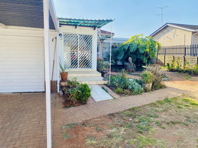 Rear exterior view featuring a paved walkway, tiled entrance steps with a security gate, and a garden area with perimeter walling.
