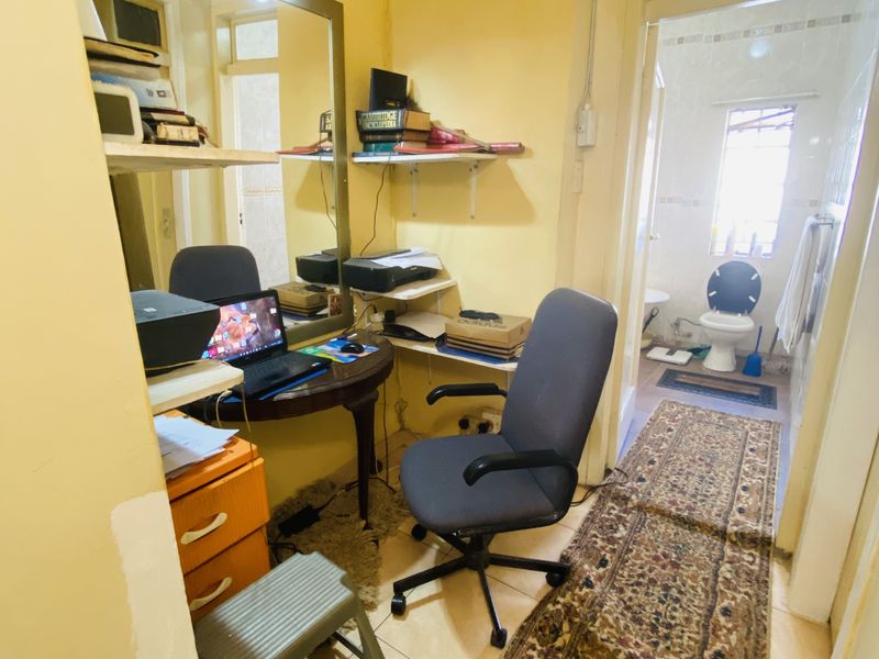 A compact home office space featuring built-in shelving and wall lighting, with direct access to an adjacent bathroom.