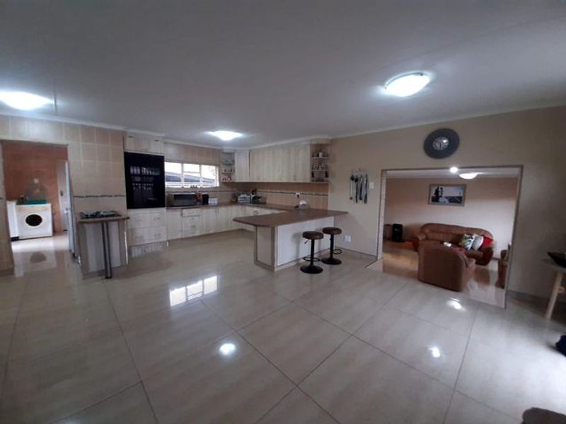 Spacious open-plan kitchen featuring light-toned cabinetry, a breakfast bar, and tiled flooring, seamlessly flowing into the adjacent living area.